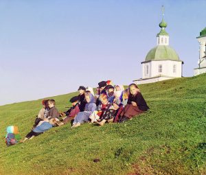 Russian children sitting on the side of a hill near a church and bell tower in the countryside near White Lake, in the north of European Russia.