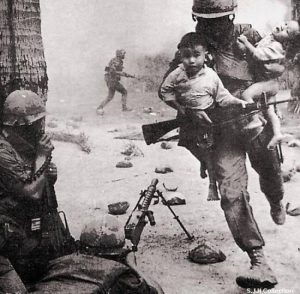 A soldier runs from the battlefield with two small Vietnamese children in his arms. [Vietnam War, c. 1955 - 1975